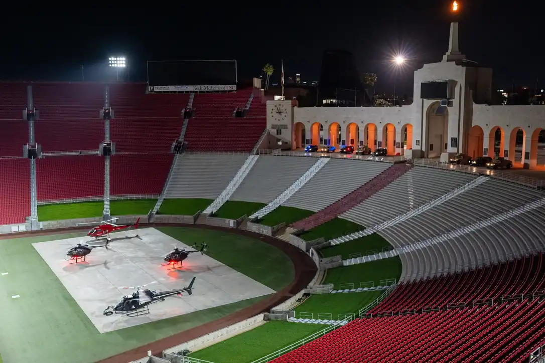 A stadium at night with four helicopters on the field and crew setting up