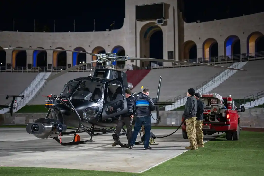 Black camera helicopter being refueled on the field of a large stadium at night