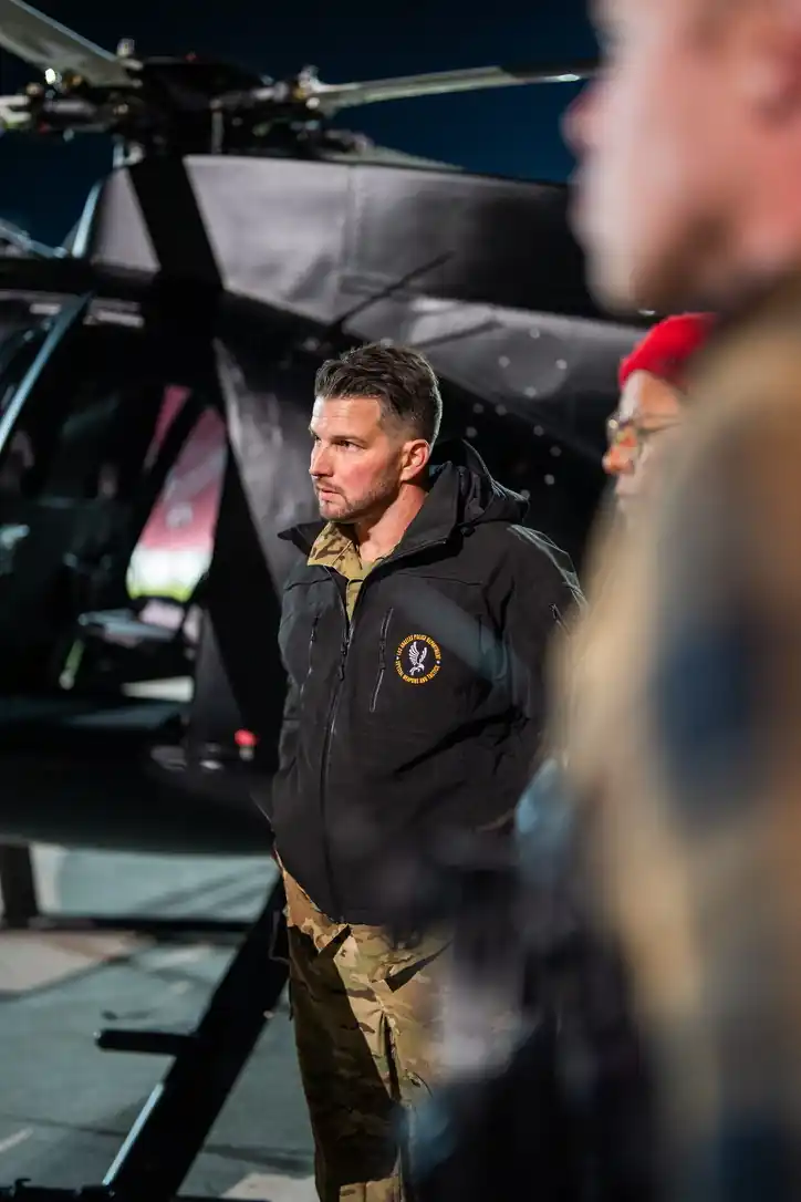 Crew member in a jacket beside a black helicopter at night