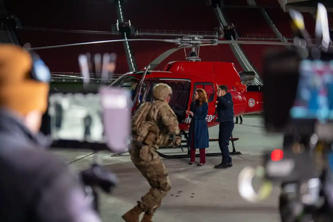 Film crew filming a scene beside a red helicopter in a stadium