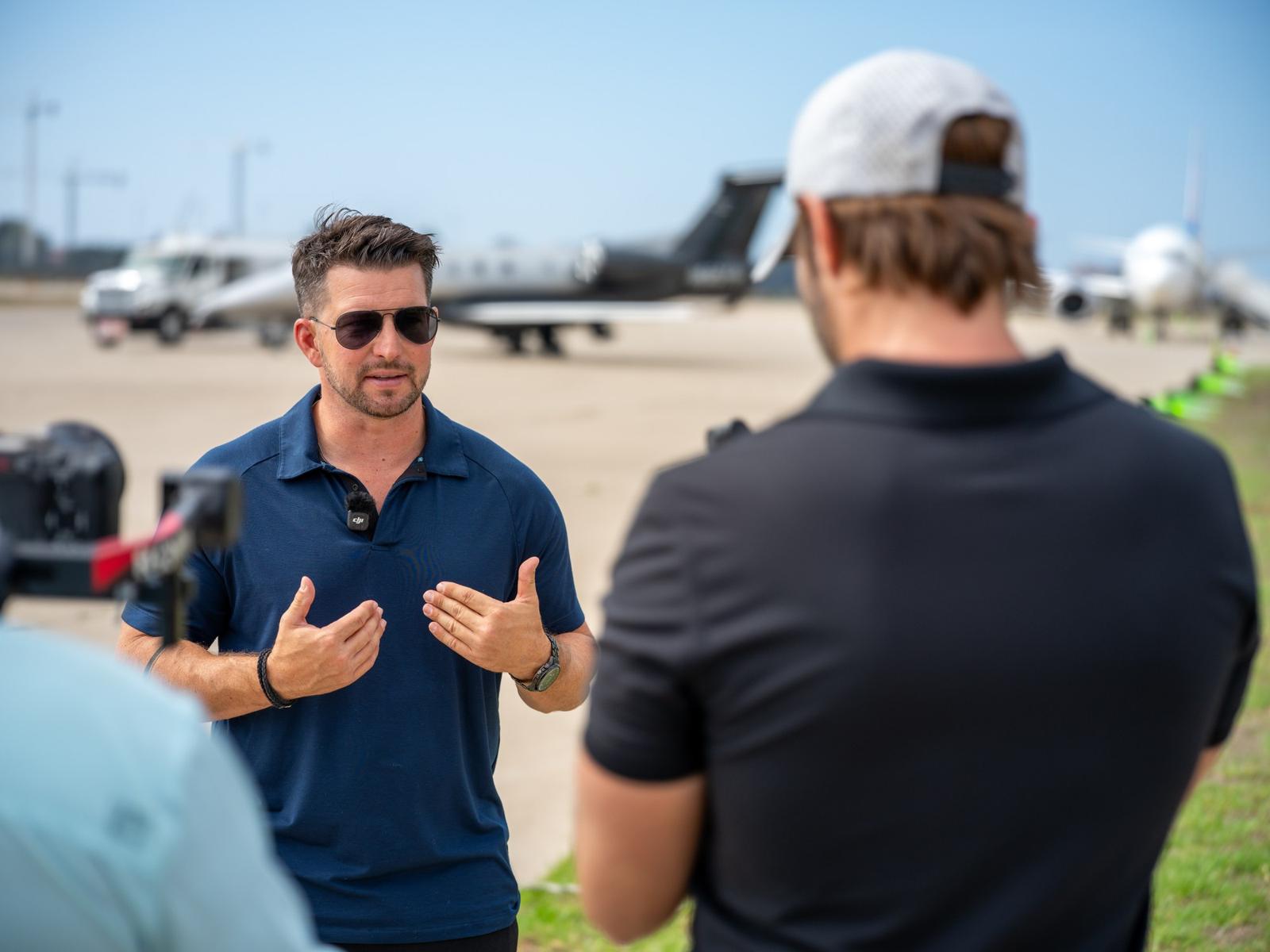 Kevin LaRosa II in sunglasses talking with a man in a cap on an airfield
