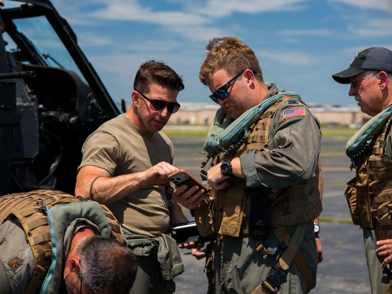 Kevin LaRosa II in sunglasses showing a phone to aircrew in flight gear beside a helicopter
