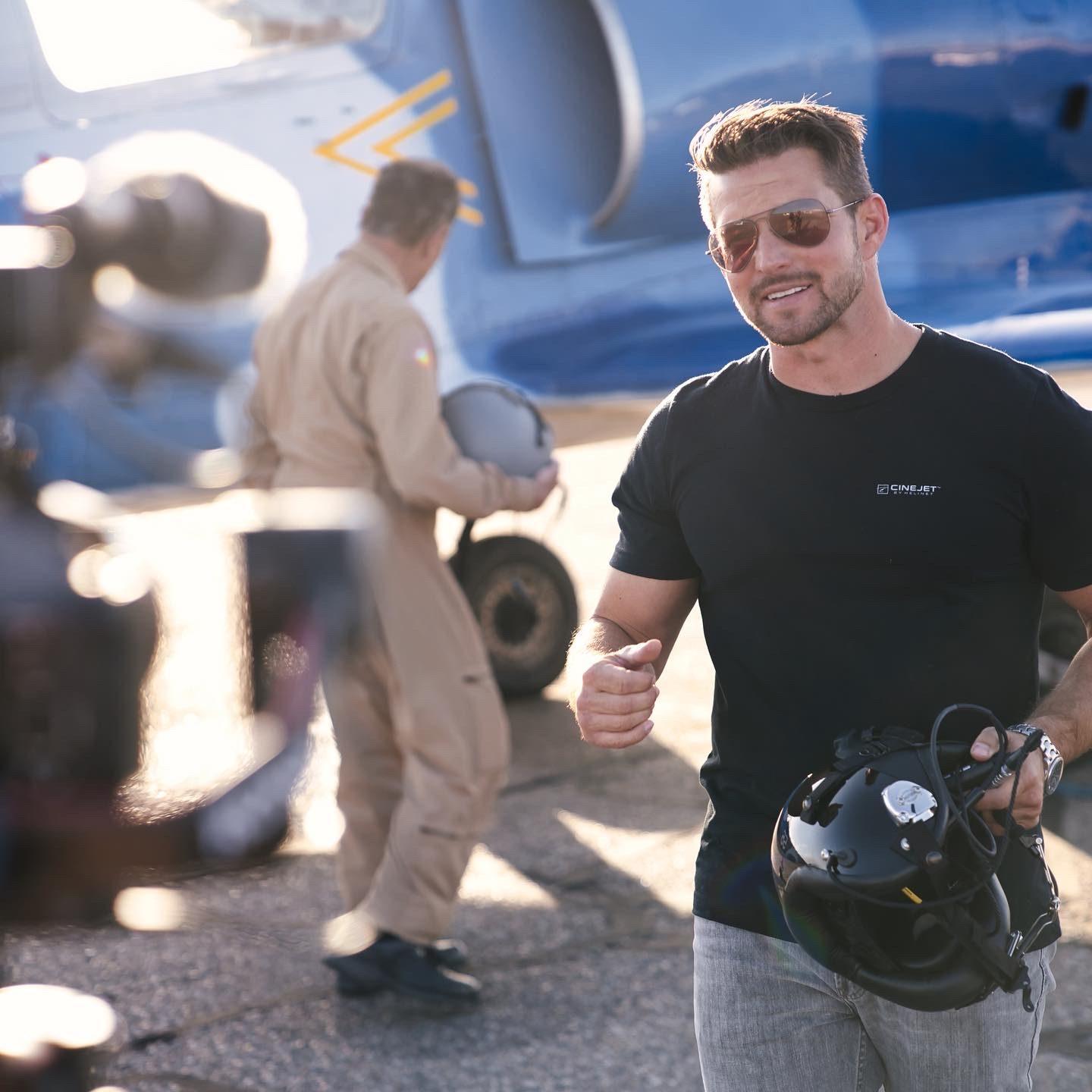 Kevin LaRosa II smiling on the ramp holding a flight helmet, a man in a flight suit behind him