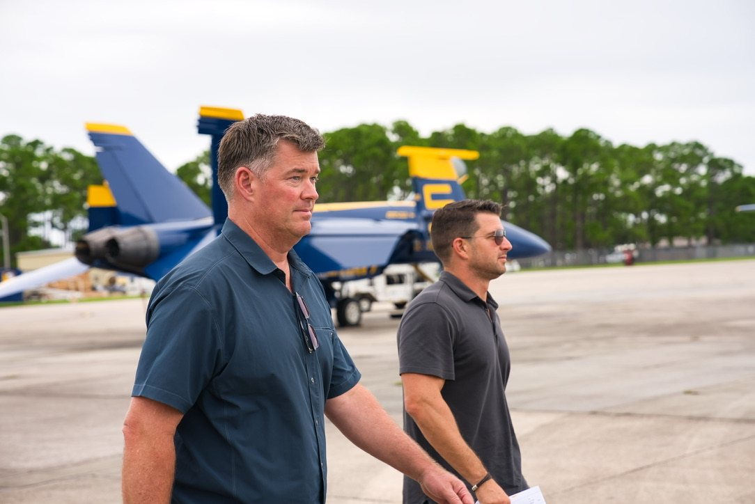 Two men walking on the flight line with Blue Angels F/A-18s behind them