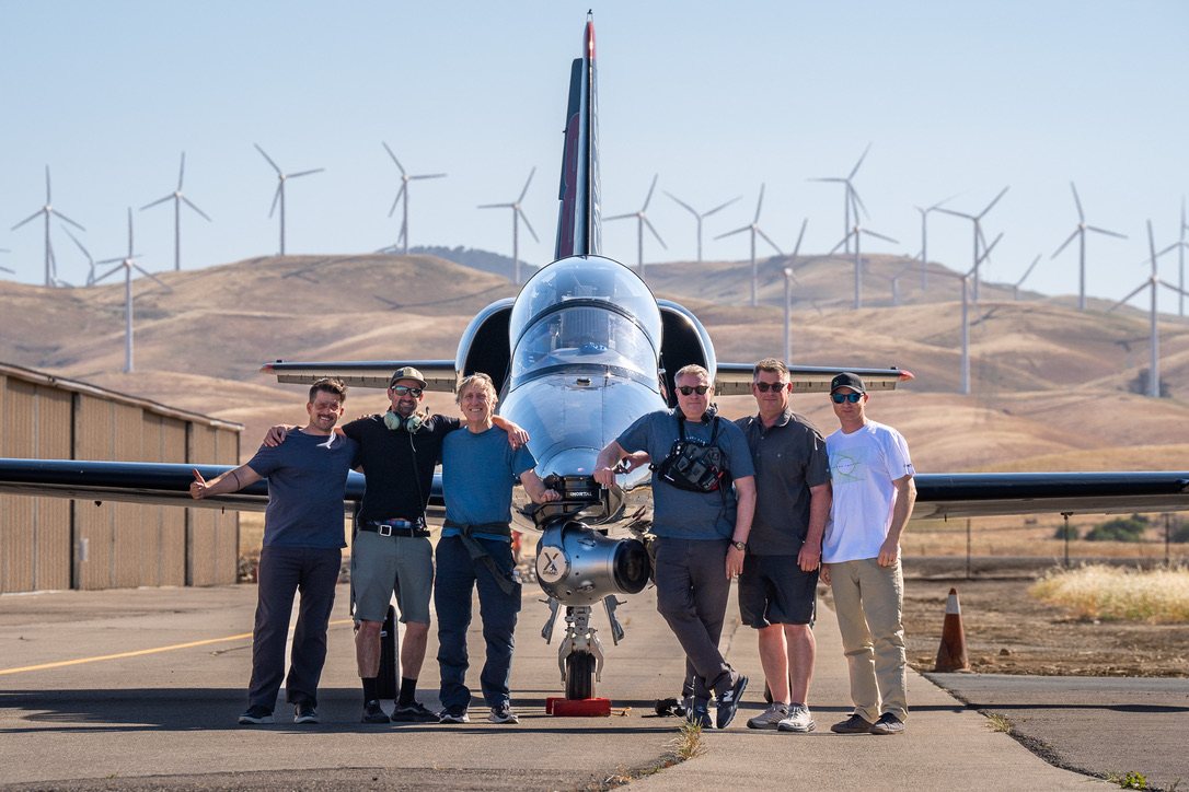 Six crew members in front of the Cinejet L-39 and its gimbal pod, wind turbines behind them