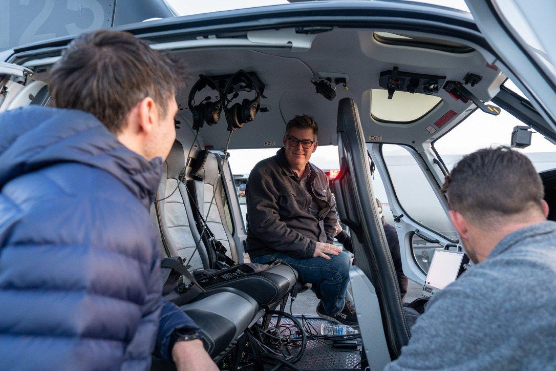 Michael FitzMaurice seated in the open cabin of an H125 helicopter, talking with two crew