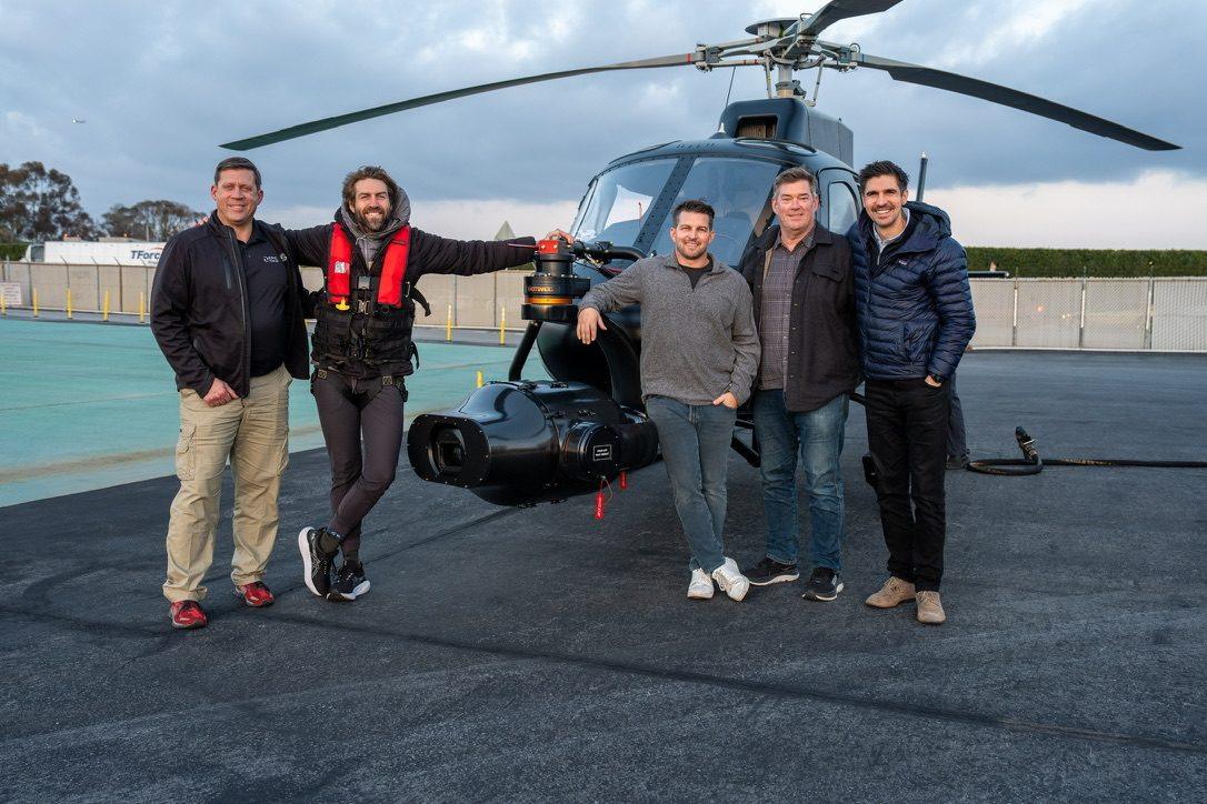 Jordan Orsak smiling with the crew in front of a camera helicopter