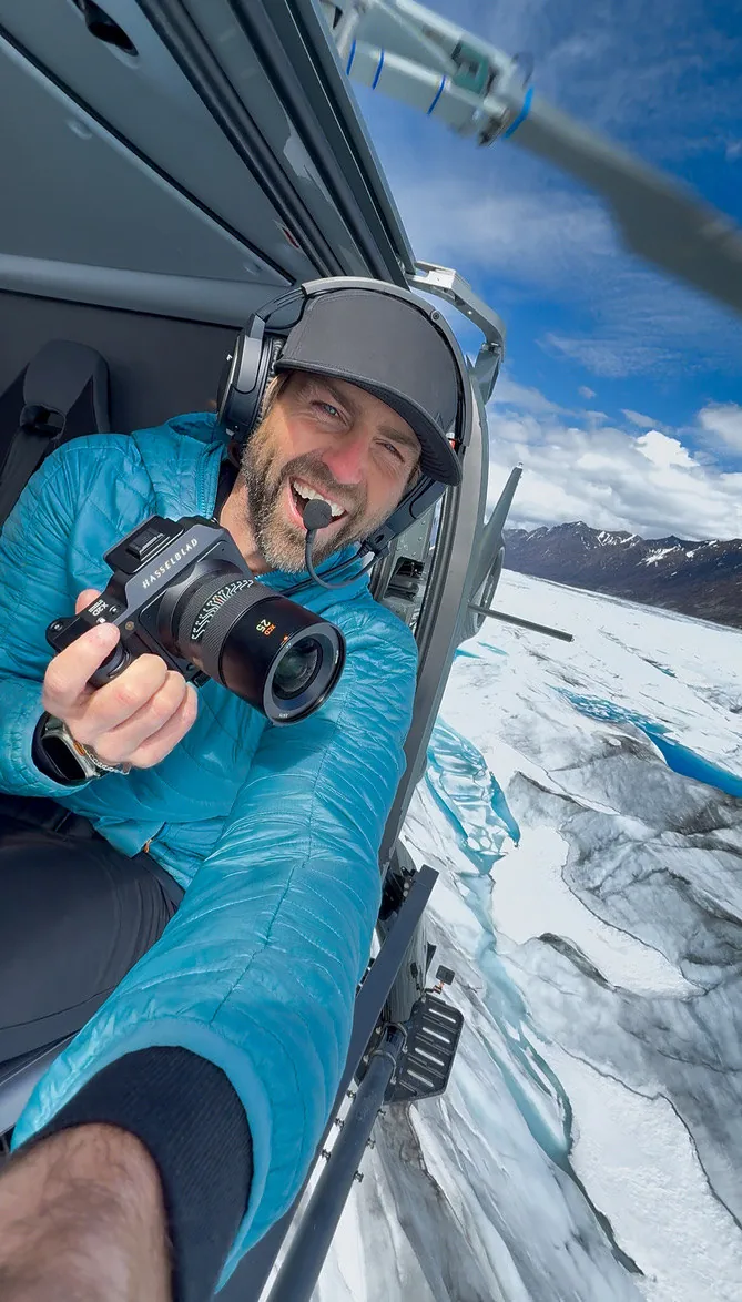 Jordan Orsak in a helicopter over a glacier, holding a Hasselblad camera