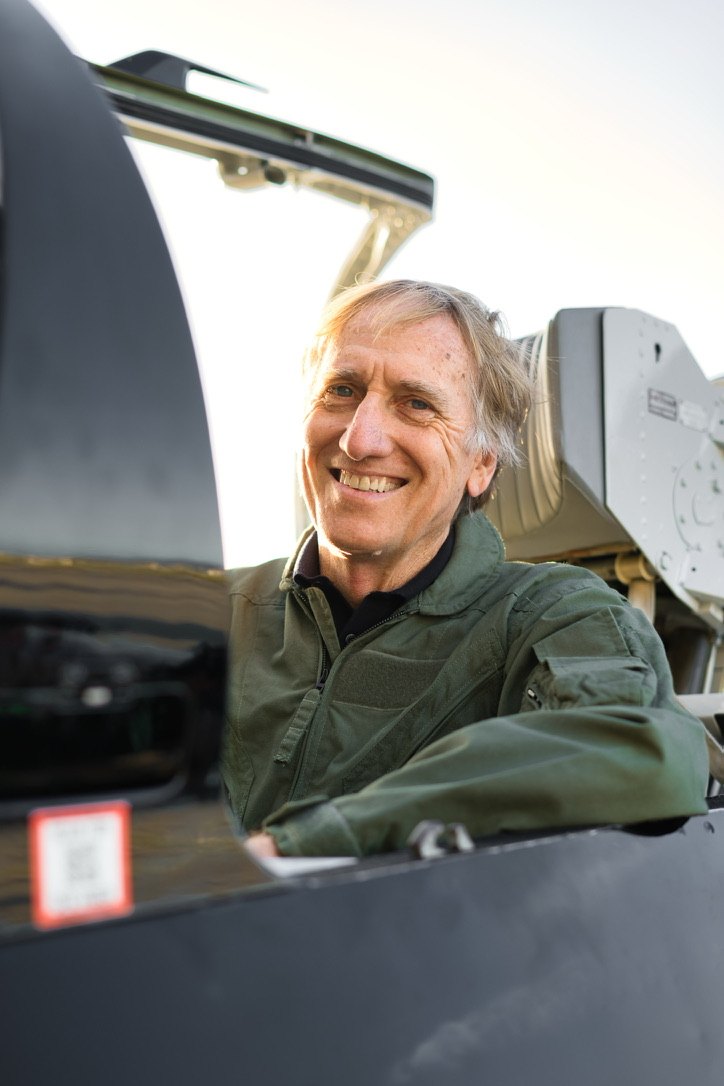 Roger Tonry smiling in a green flight jacket in a jet cockpit